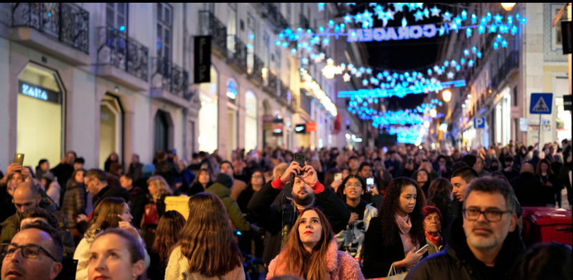 People look up at Christmas lights as crowds stroll around downtown Lisbon’s Chiado neighborhood